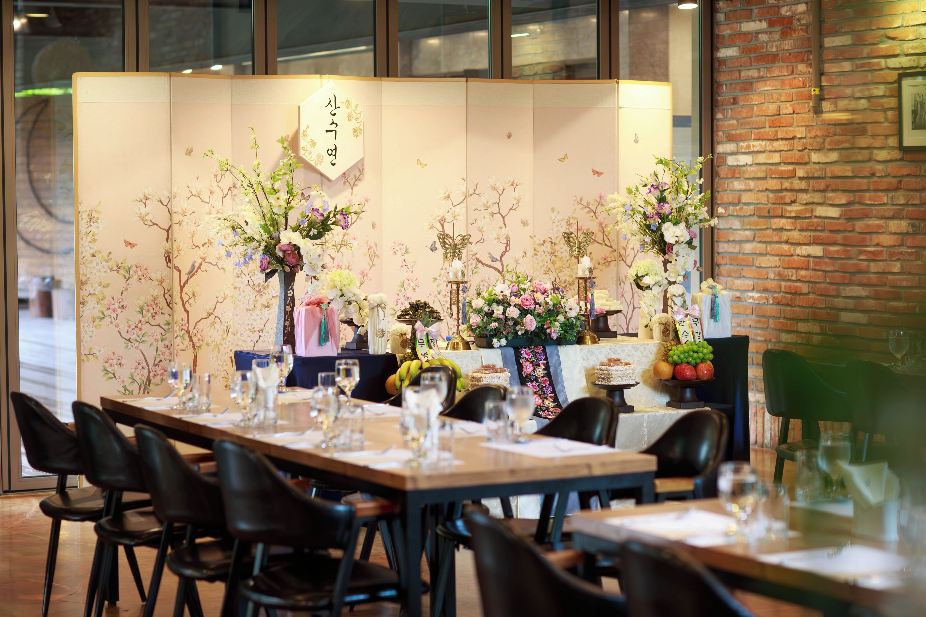 A restaurant interior with a long dining table set for a meal, chairs, and a decorative backdrop with floral arrangements.