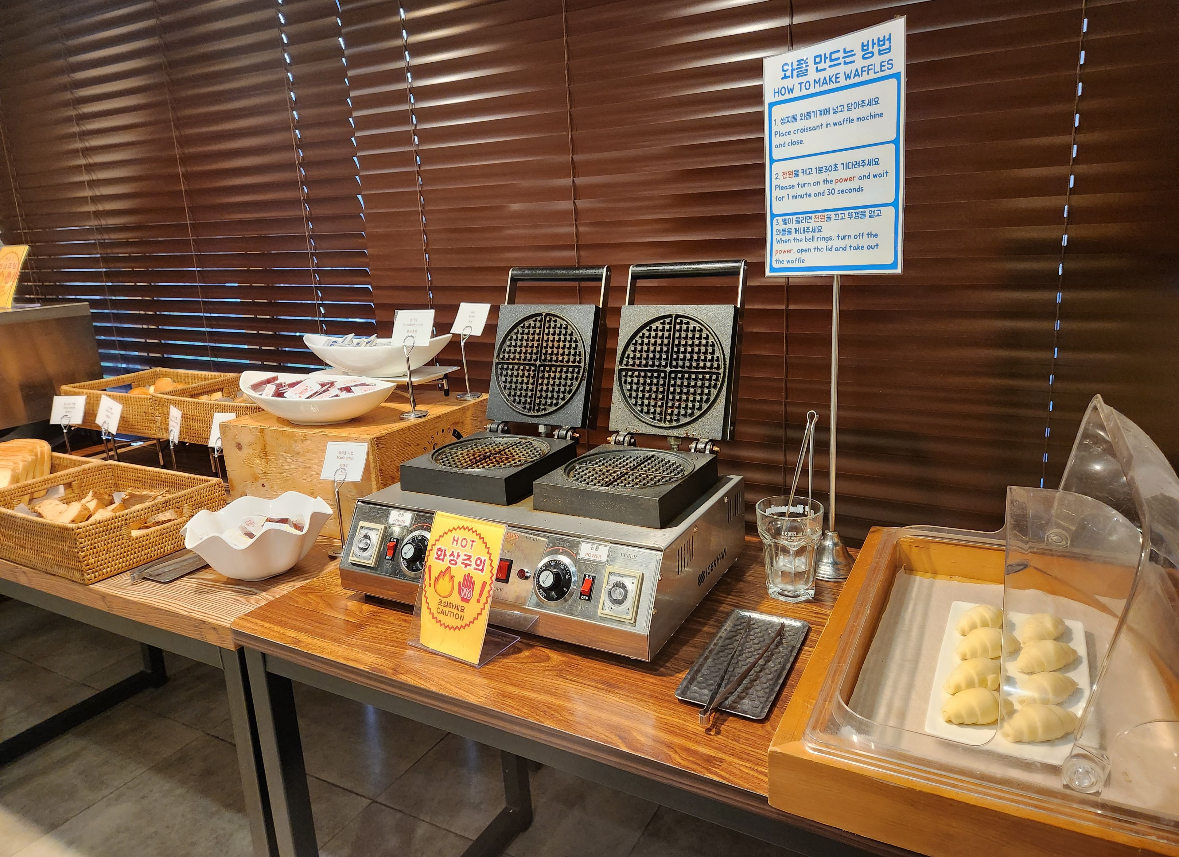A waffle station with instructions, a waffle maker, and various bread and pastry items.