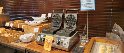 A waffle station with instructions, a waffle maker, and various bread and pastry items.