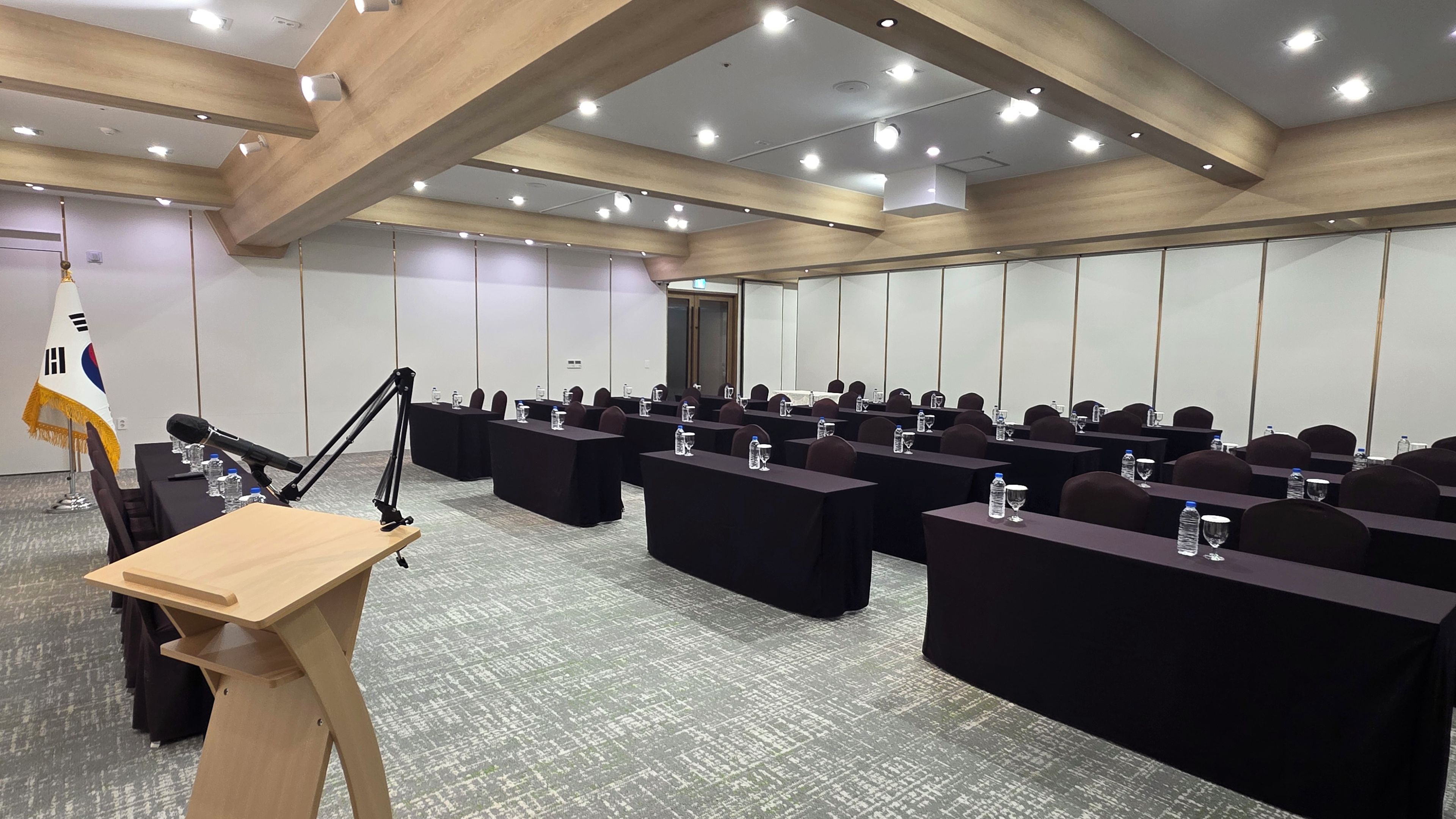 Un salón de conferencias con mesas, sillas, un atril y una bandera.
