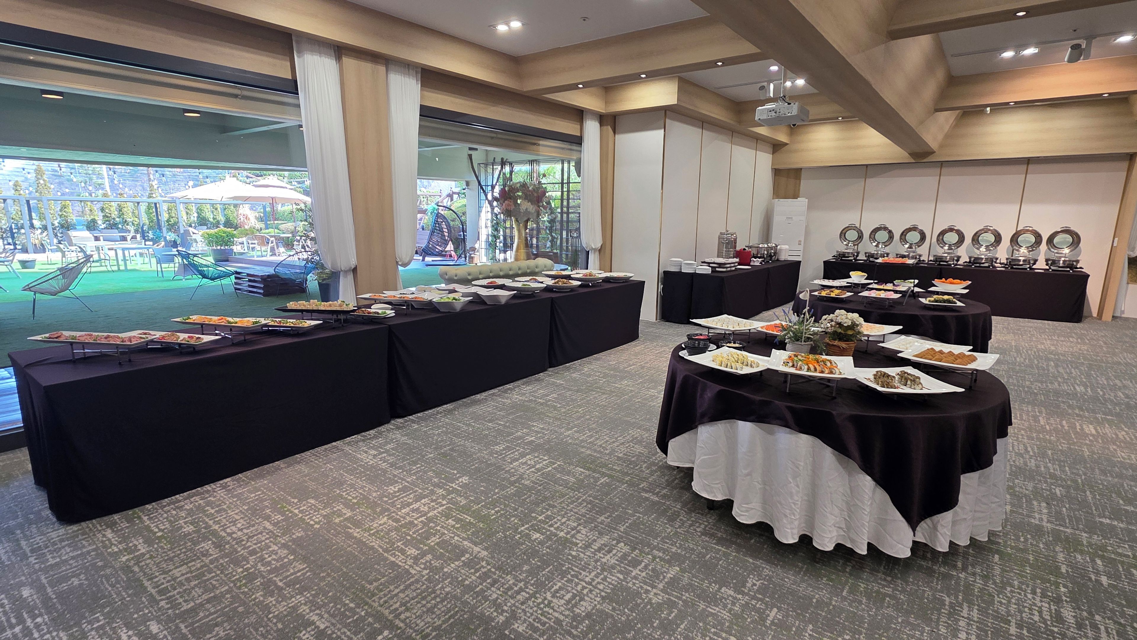 A buffet setup with multiple tables covered in black cloths, featuring an array of dishes.