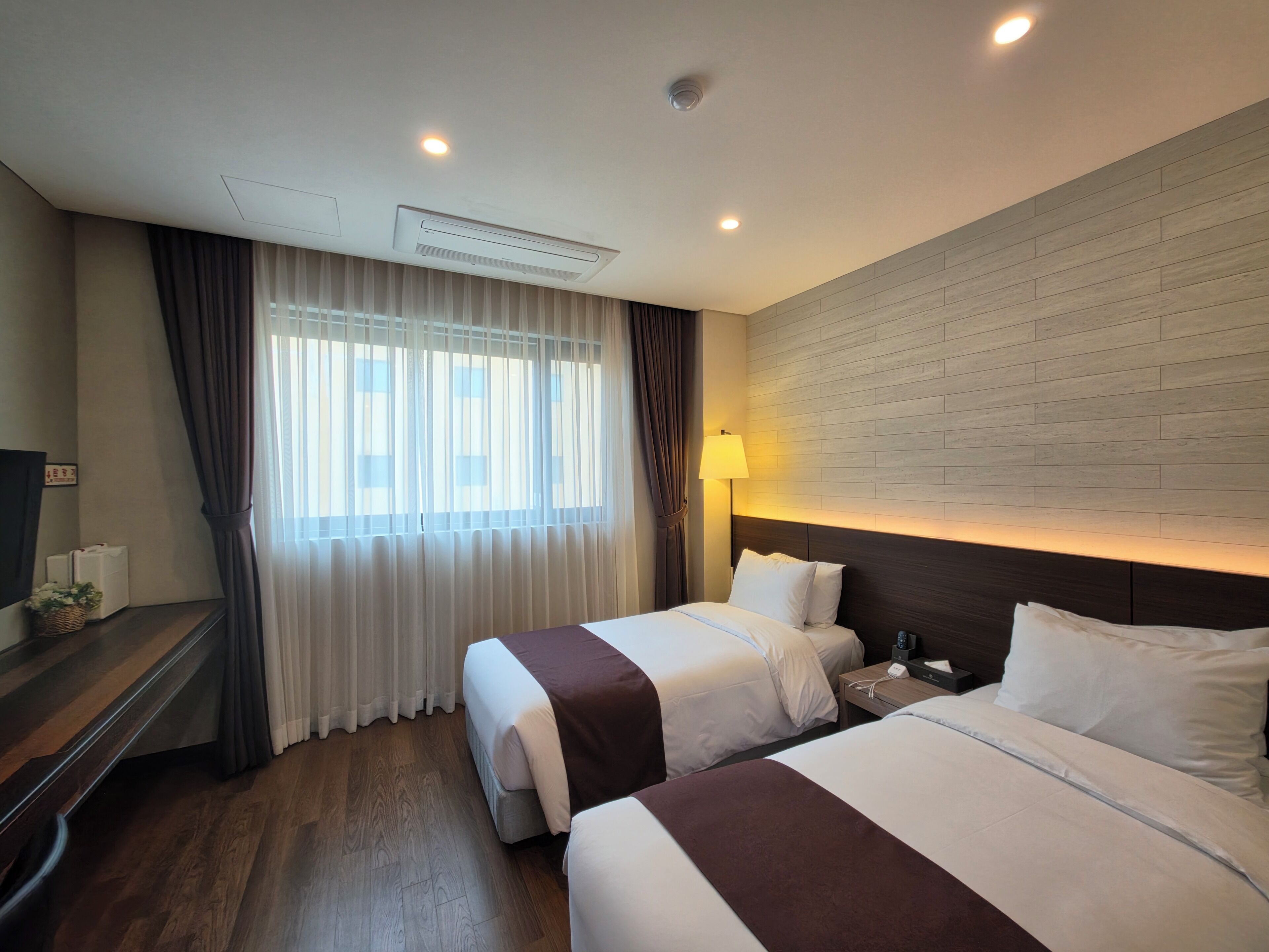 A hotel room with two beds, a TV, a desk, and a window with curtains.