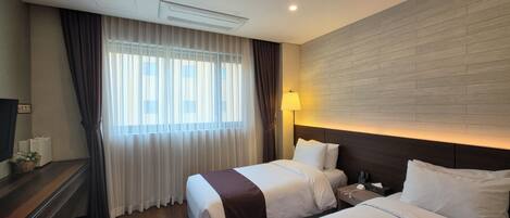 A hotel room with two beds, a TV, a desk, and a window with curtains.