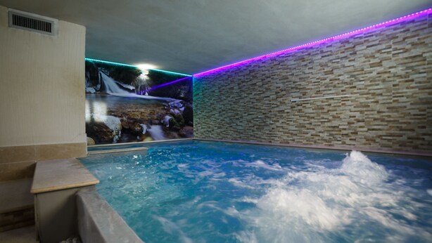 A spa area with a hot tub, stone walls, and a waterfall feature. - Olympic Regina Hotel (Giustino)