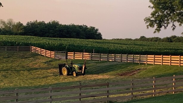 Een tractor in een veld met een houten omheining.