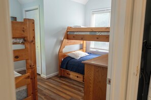 Un lit superposé avec une tête de lit et un pied de lit en bois, un lit simple avec une couvre-lit bleue et un bureau en bois doté de tiroirs.