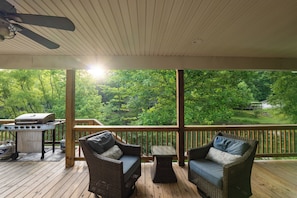 Un espace extérieur abrité, aménagé avec des meubles en osier, un barbecue et offrant une vue sur un paysage boisé.