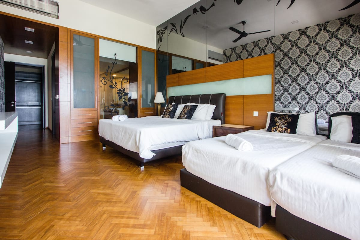A hotel room with two beds, wooden flooring, a large mirror, and a patterned wall.