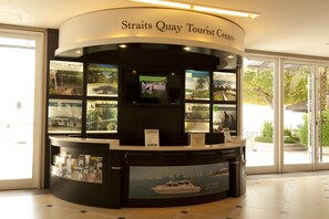 A tourist center with a curved reception desk, informational displays, and a large window offering a view of the outdoors. - Profolio Straits Quay (George Town)