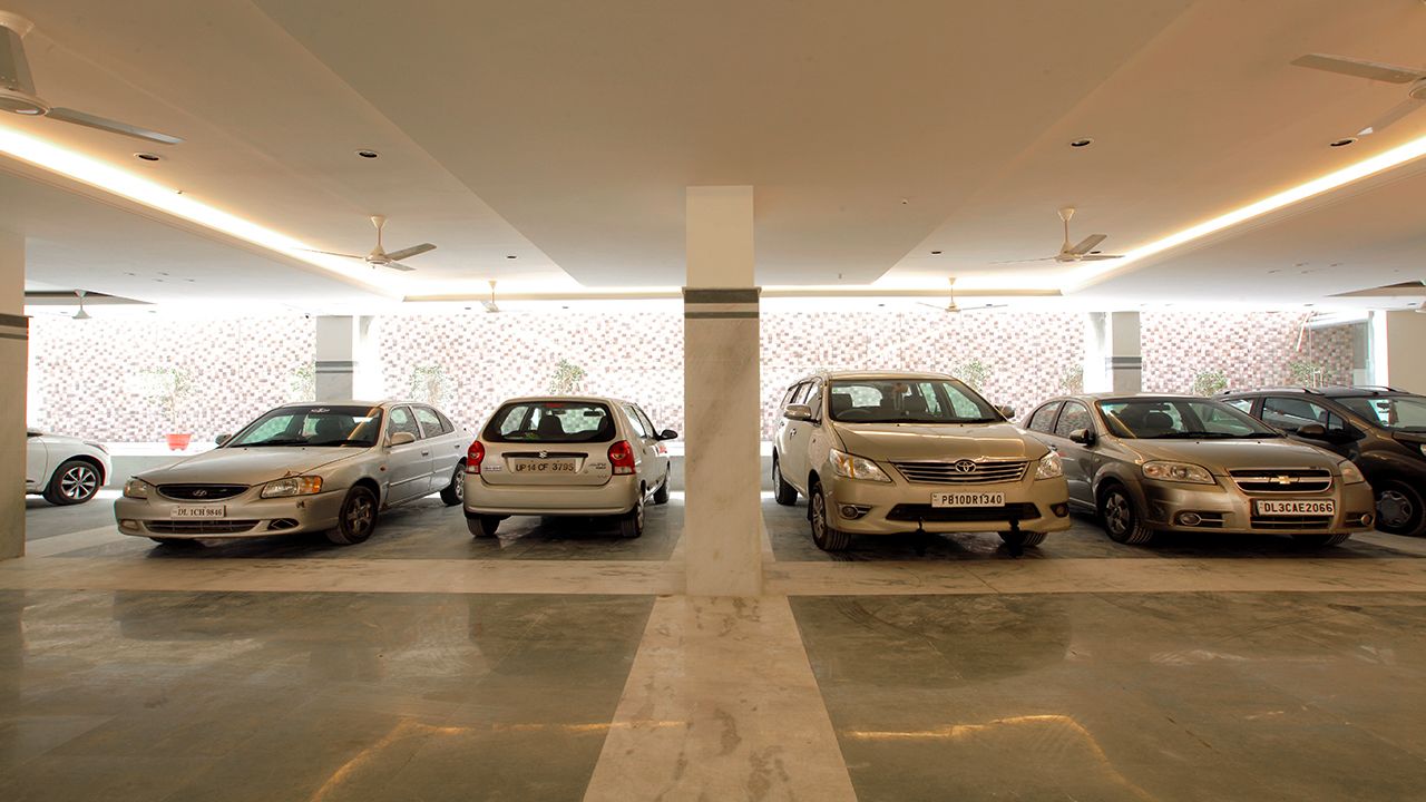 Un aparcamiento con varios coches estacionados en filas, un pilar central y una pared con diseño al fondo.