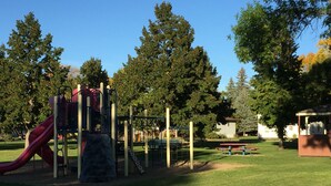 Un parque infantil con tobogán y estructuras para escalar, rodeado de árboles y una zona de picnic.