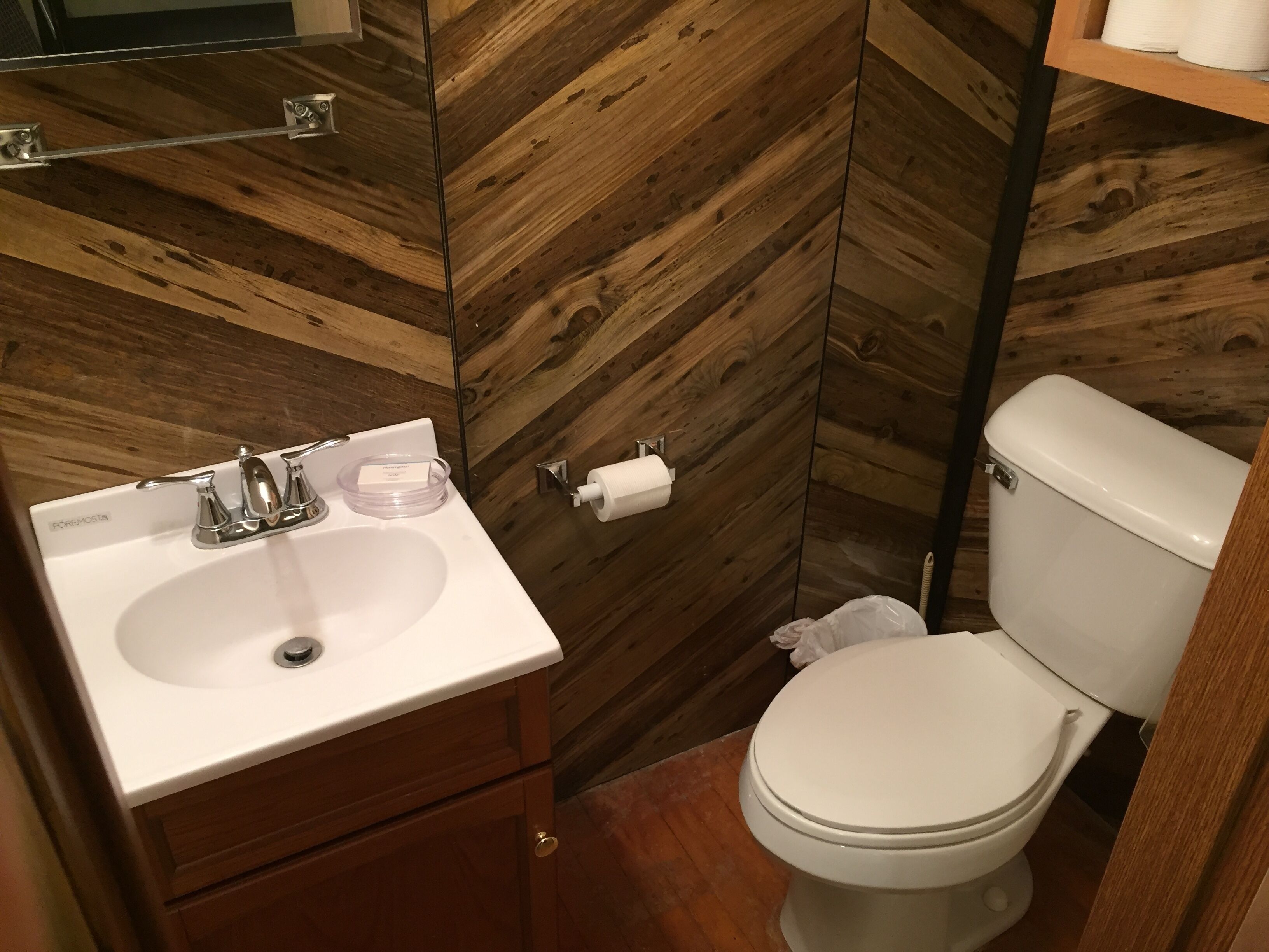 Une salle de bain avec un mur recouvert de panneaux en bois, un lavabo blanc avec un robinet chromé et des toilettes.