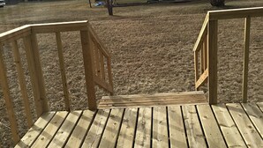 Una terraza de madera con una rampa que baja a un jardín cubierto de césped.
