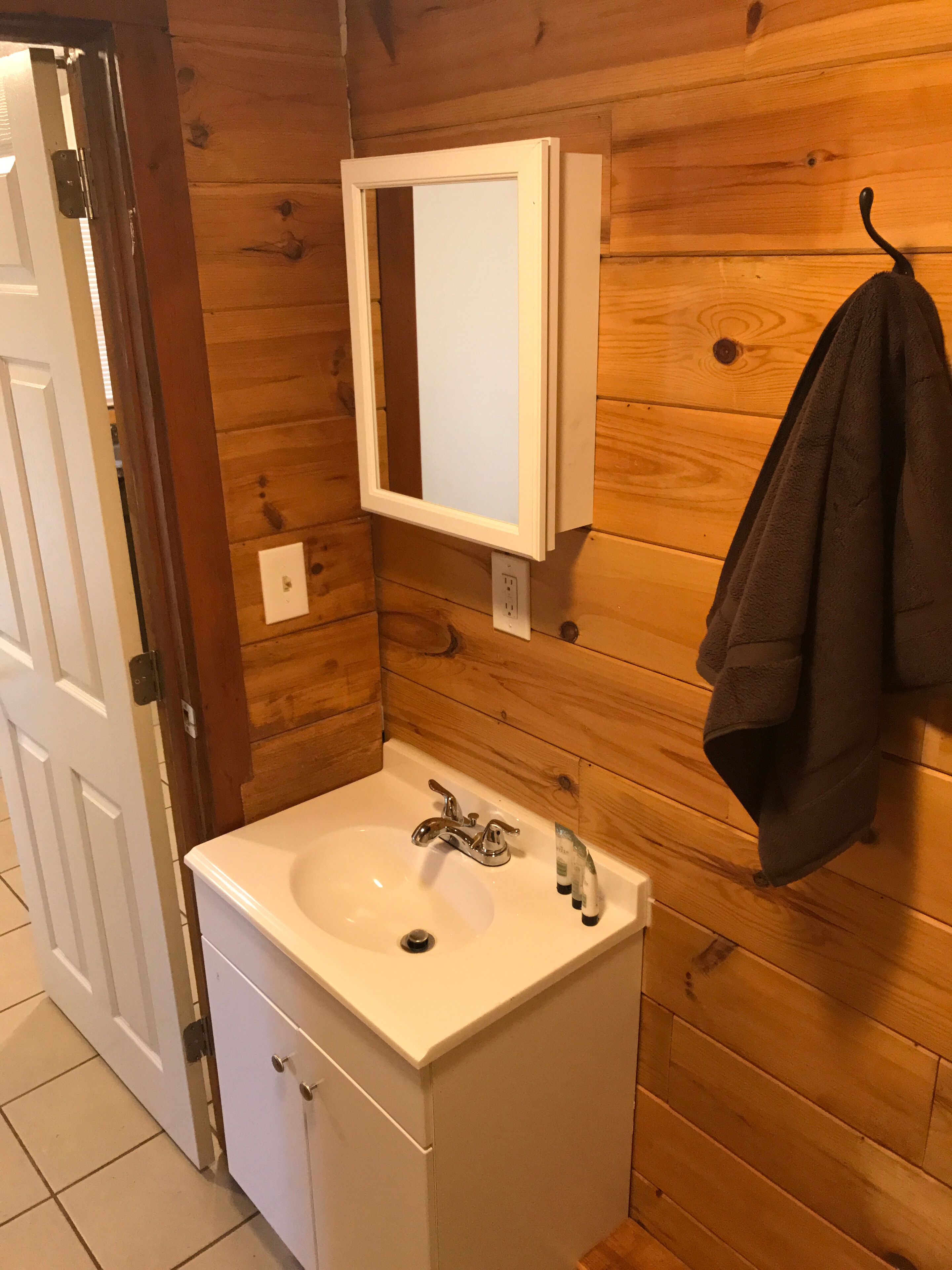 Une salle de bain avec un lavabo blanc, un miroir et des murs en bois.