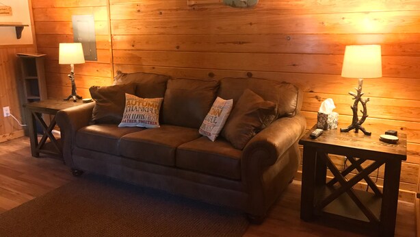 Una habitación acogedora con un sofá de cuero, dos mesitas de noche con lámparas y una pared de madera.