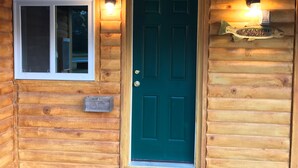 Una cabaña de madera con puerta verde, una ventana y un cartel en la puerta.