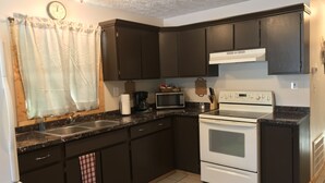 Una cocina con gabinetes oscuros, una estufa blanca, un microondas y un fregadero.