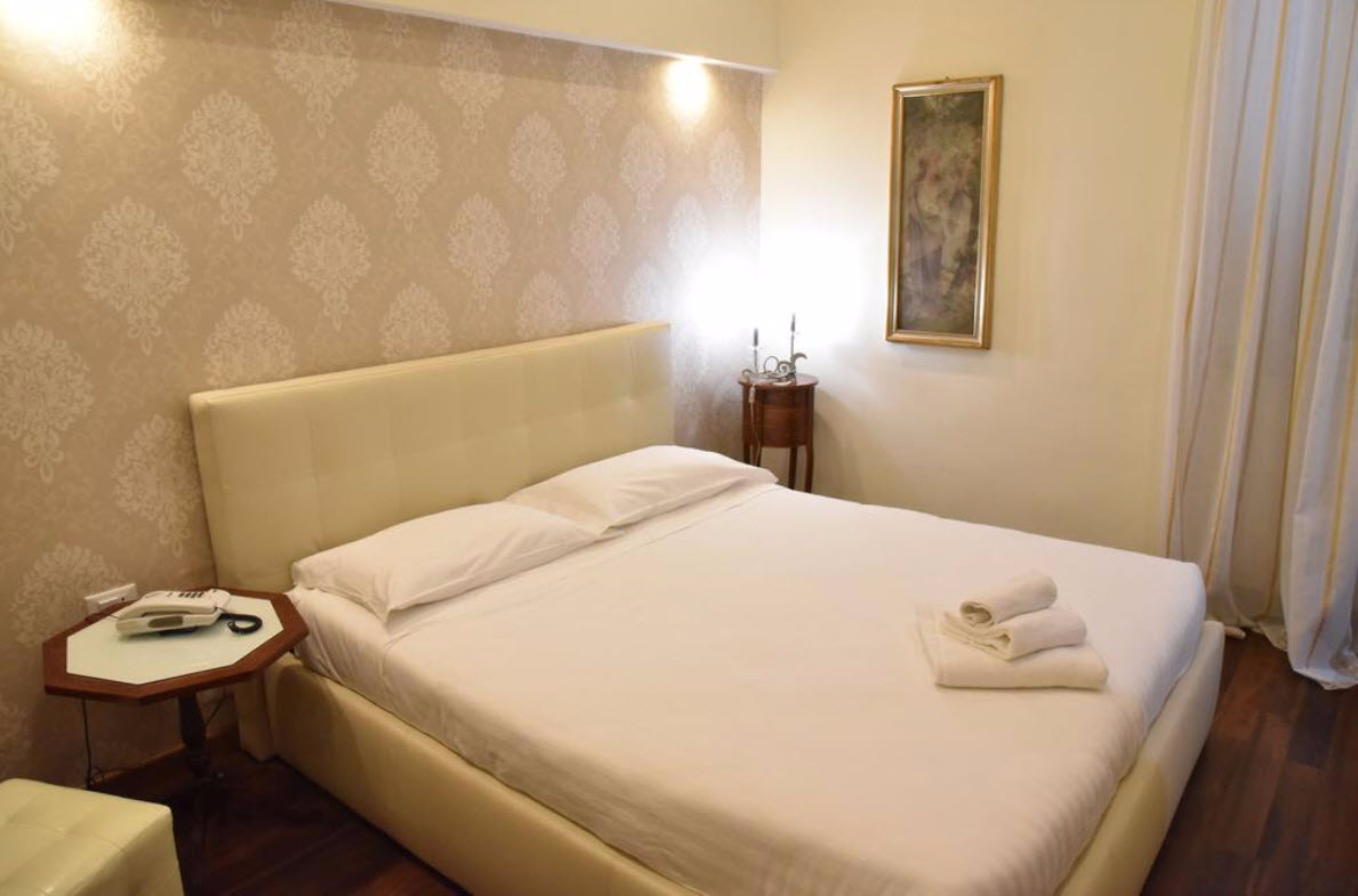 Una cama bien hecha con sábanas blancas y una toalla doblada al lado.