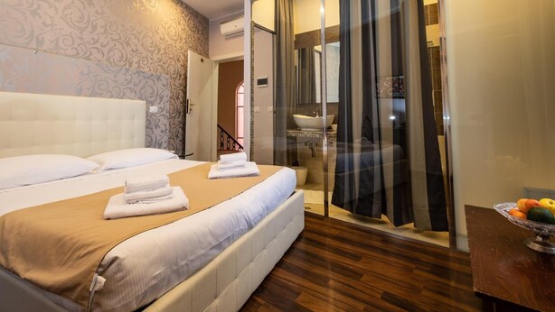 A hotel room with a large bed, a glass shower enclosure, and a fruit bowl on a wooden table. - Antico Hotel Moderno (Piombino)