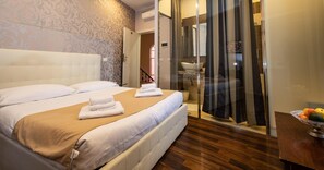 A hotel room with a large bed, a glass shower enclosure, and a fruit bowl on a wooden table. - Antico Hotel Moderno (Piombino)