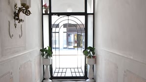 A hallway with a red carpet, white walls, and a black-framed window leading to a bright room. - Antico Hotel Moderno (Piombino)