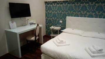 A hotel room with a bed, a desk, a chair, a small round table, and a television mounted on the wall.