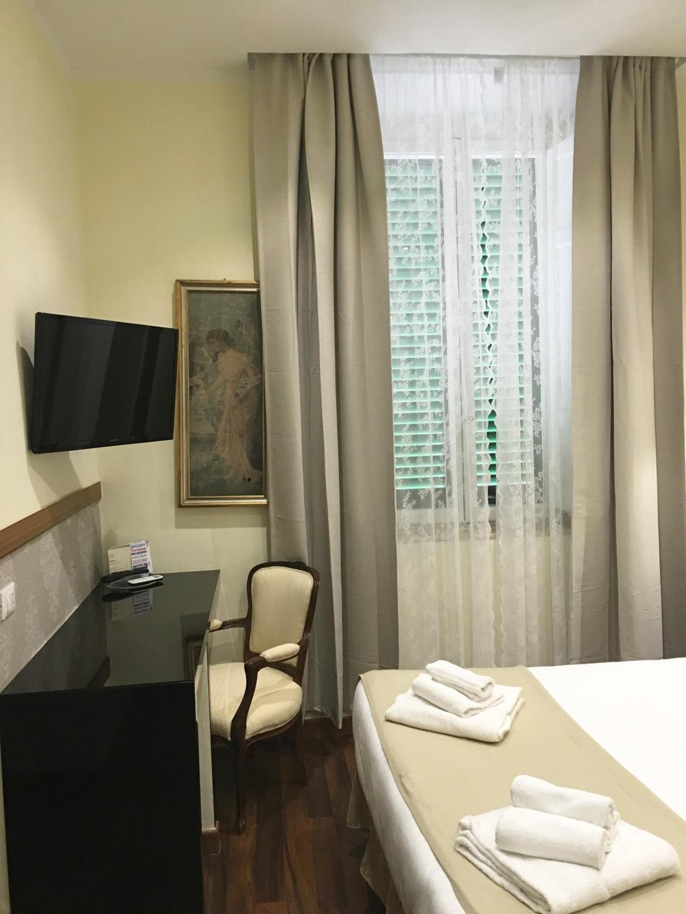 Une chambre d’hôtel comprenant un lit, un bureau avec une chaise, un téléviseur fixé au mur et une fenêtre avec des rideaux.