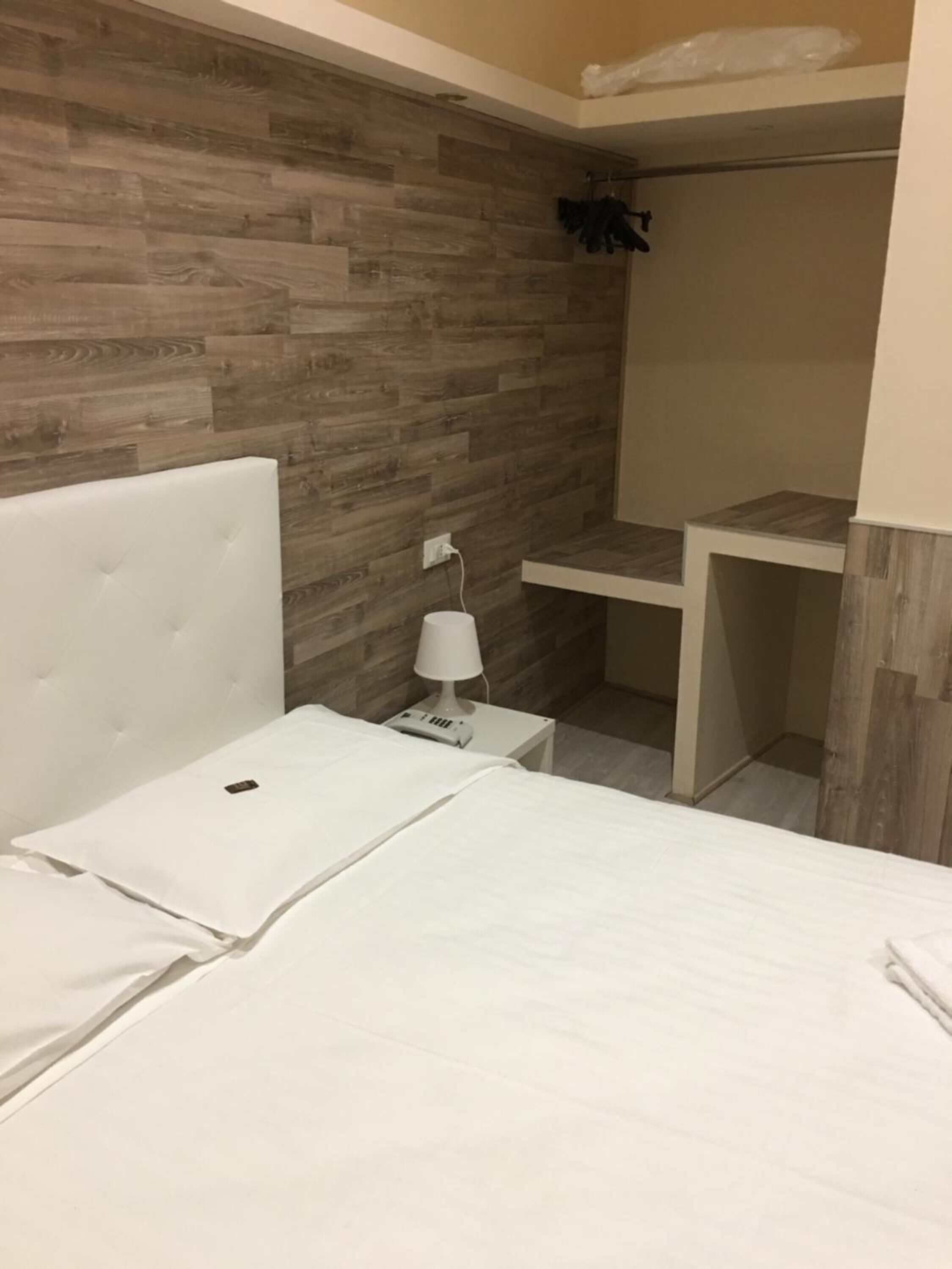 A bedroom with a white bed, a nightstand with a lamp, and a wooden wall.