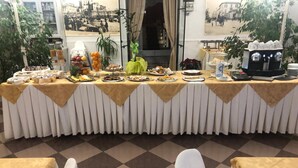 A buffet table with various food items and a coffee machine, set against a checkered floor and a view of a street scene through a window. - Antico Hotel Moderno (Piombino)