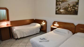 Habitación de hotel con dos camas individuales, cabecero de madera, mesita de noche con lámpara, teléfono y un cuadro en la pared.
