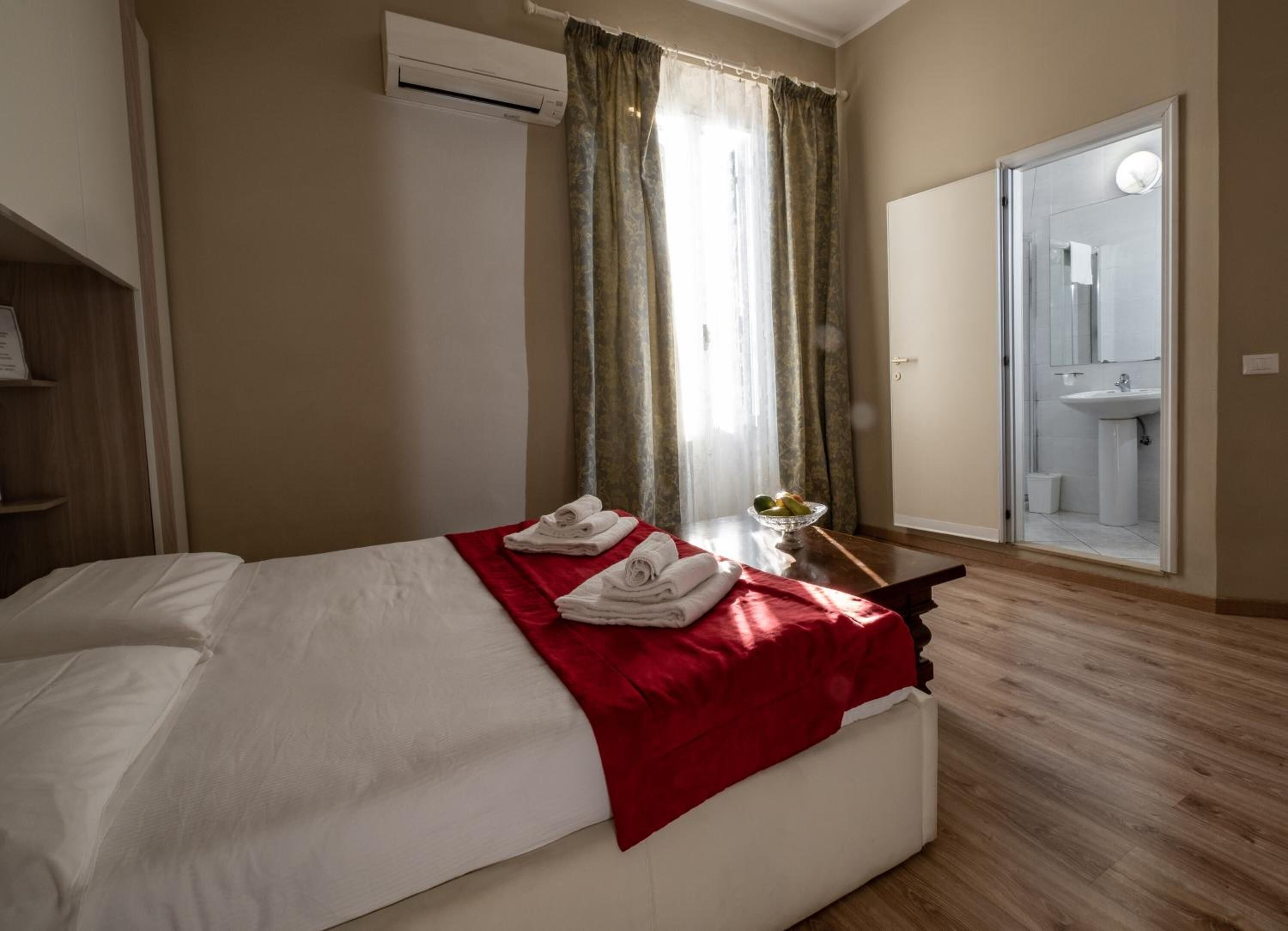 Habitación de hotel con una cama, una mesita de noche con toallas, un frutero y vista al baño.