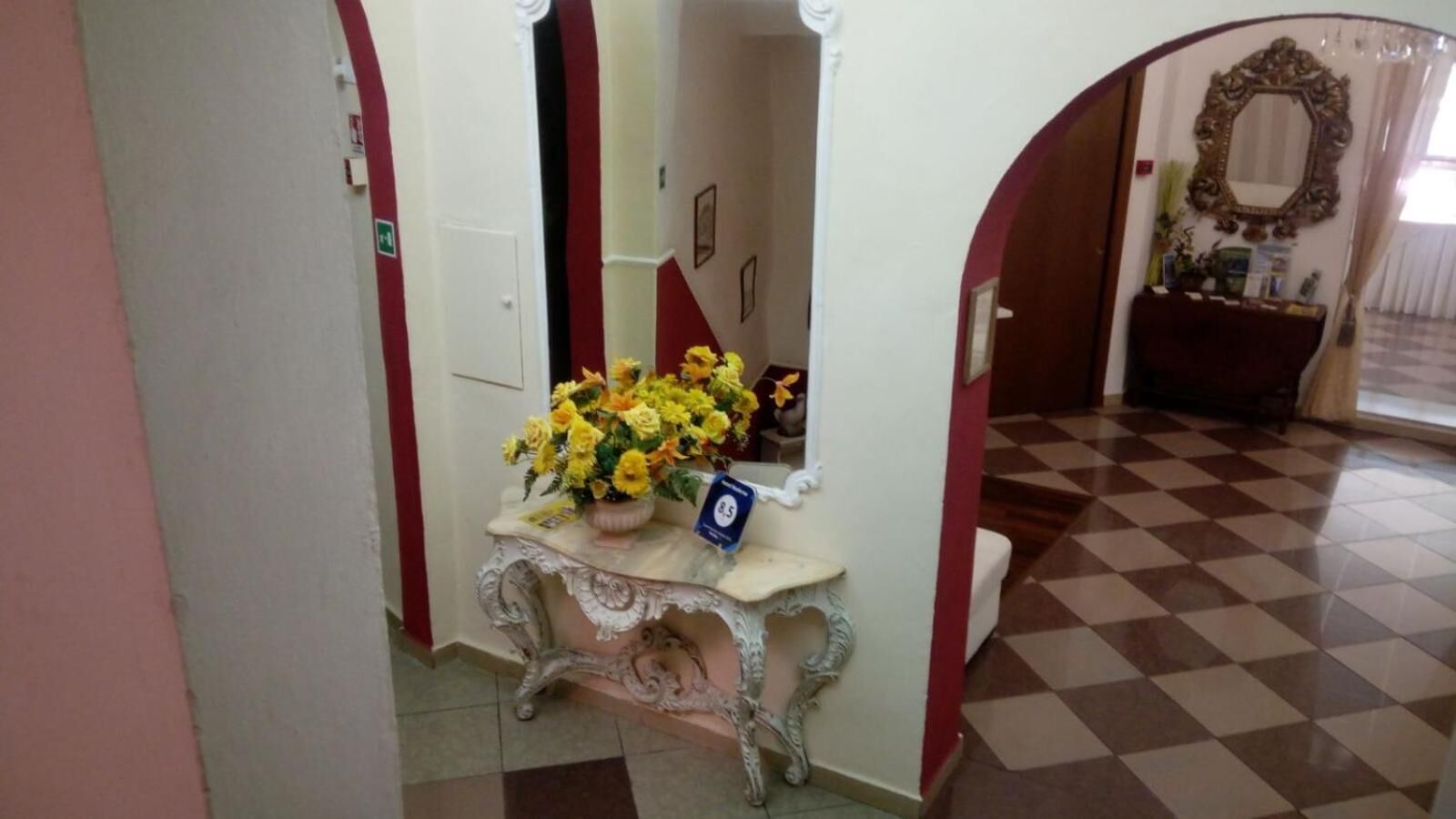 A hallway with a decorative console table holding a vase of yellow flowers, a blue sign, and a mirror on the wall.