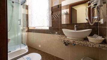 A bathroom with a glass-enclosed shower, a white sink with a mosaic tile backsplash, and a toilet with a blue symbol on the lid.