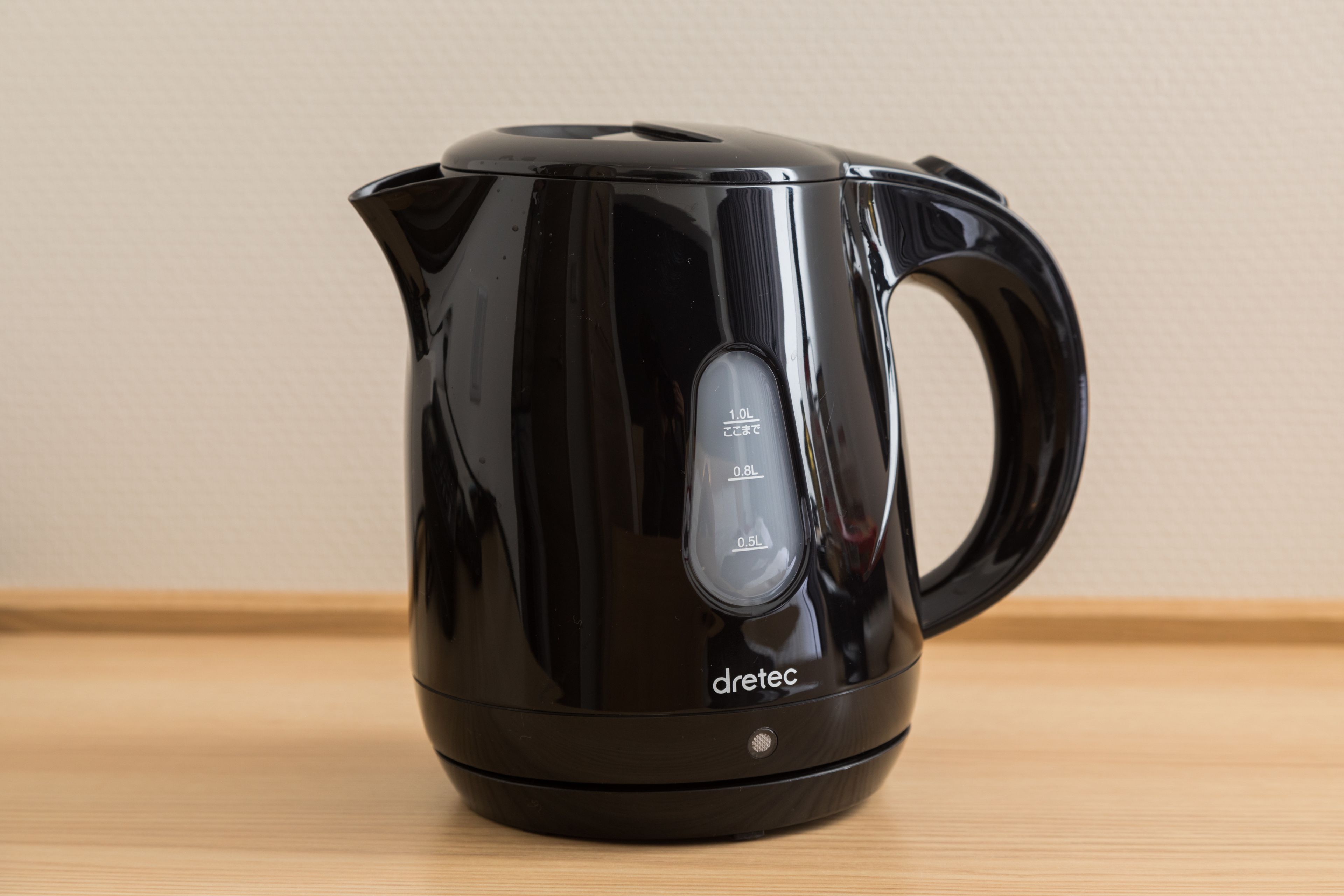 Ein schwarzer Wasserkocher mit Henkel und Ausguss auf einer Holzoberfläche.