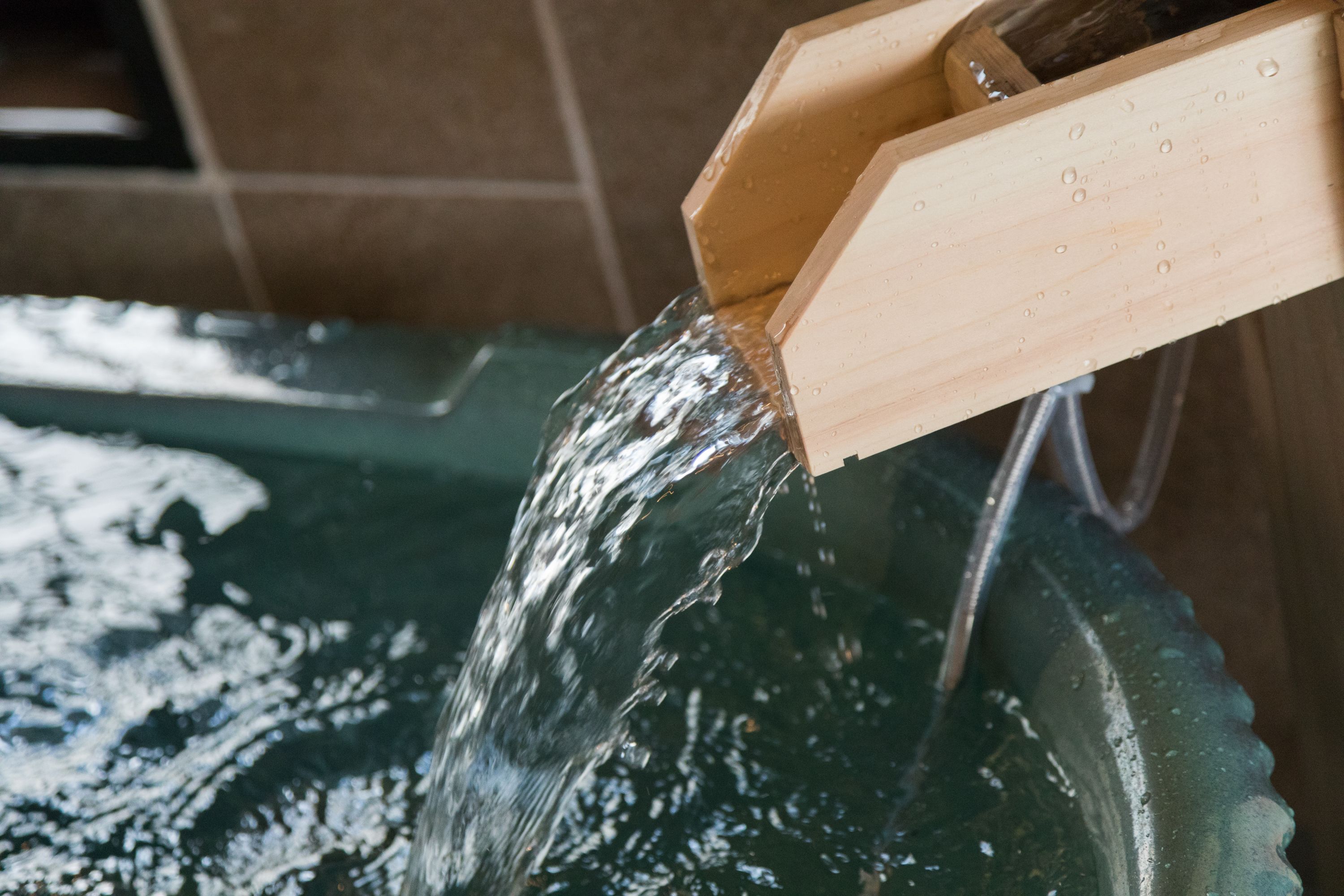 A wooden water spout pouring water into a glass bowl.