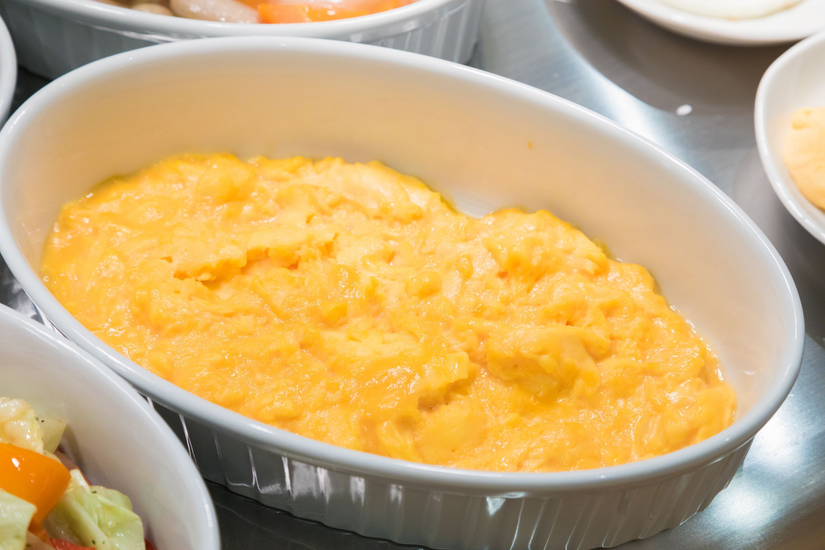 A white oval dish with a creamy yellow substance, possibly a dessert, on a metallic surface.