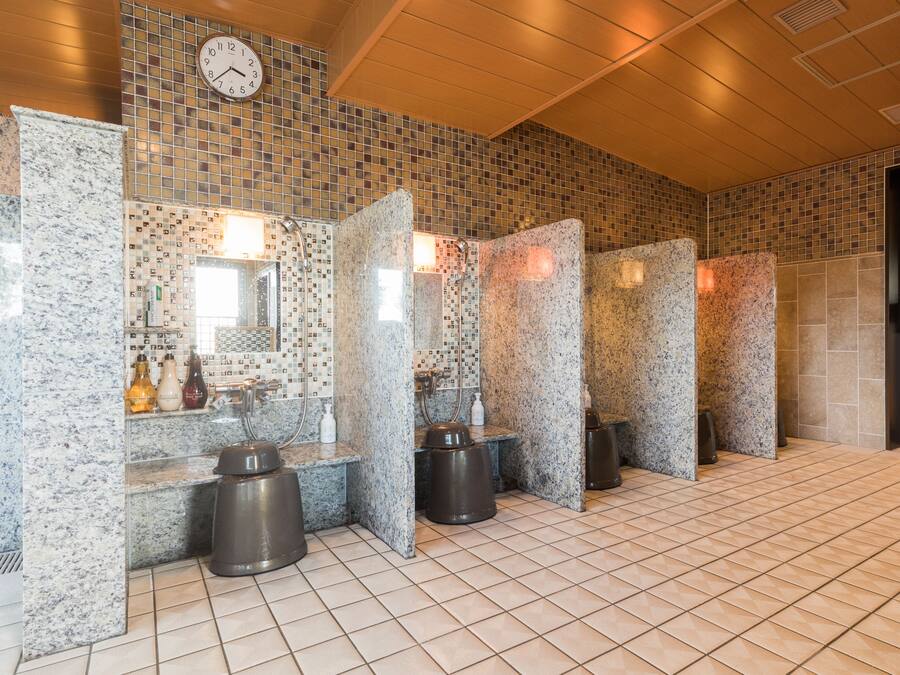 A public restroom with tiled walls, granite counters, and a clock on the wall.