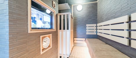Een hotelkamer met een bakstenen muur, een houten bankje, een klok en een raam met uitzicht op de straat.