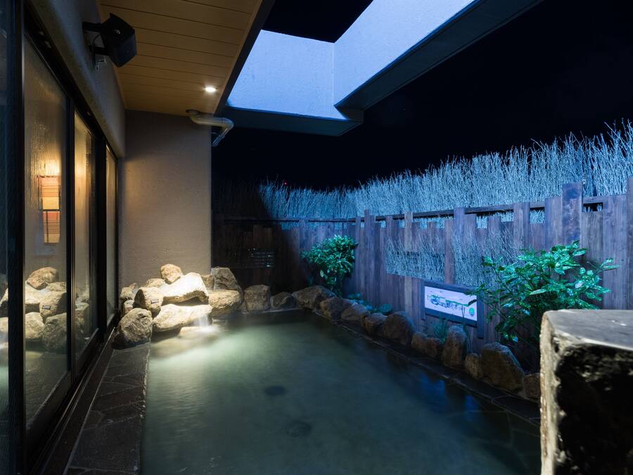 A tranquil indoor garden with a water feature, wooden fence, and potted plants.