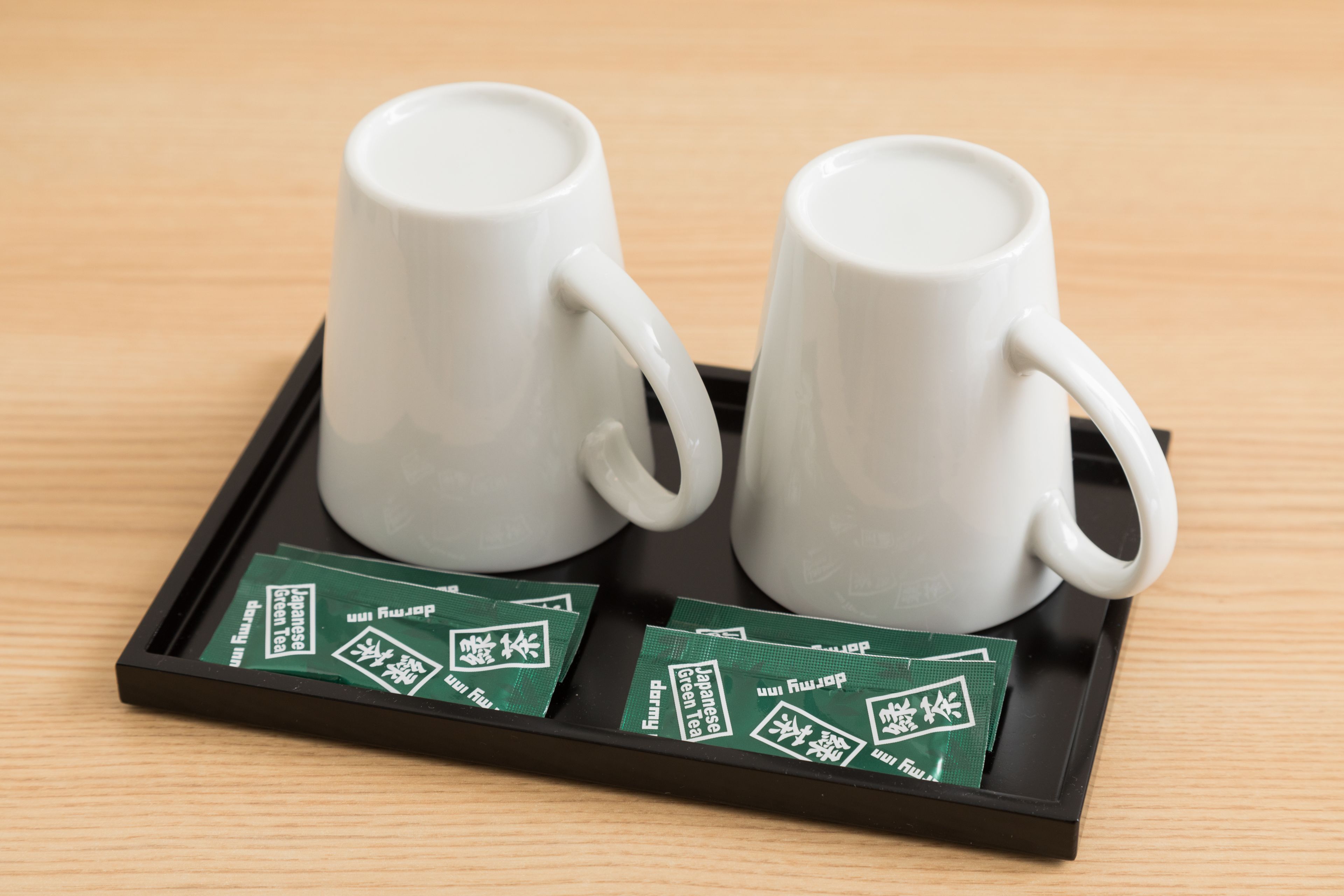 Two white ceramic cups on a black tray with green tea packets.