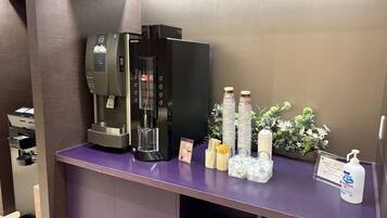 En selvbetjeningskaffestation med kaffemaskine, papkrus og en vanddispenser.
