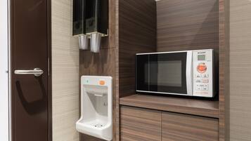Un four à micro-ondes posé sur un meuble en bois, un sèche-mains et une porte dotée d’une poignée.