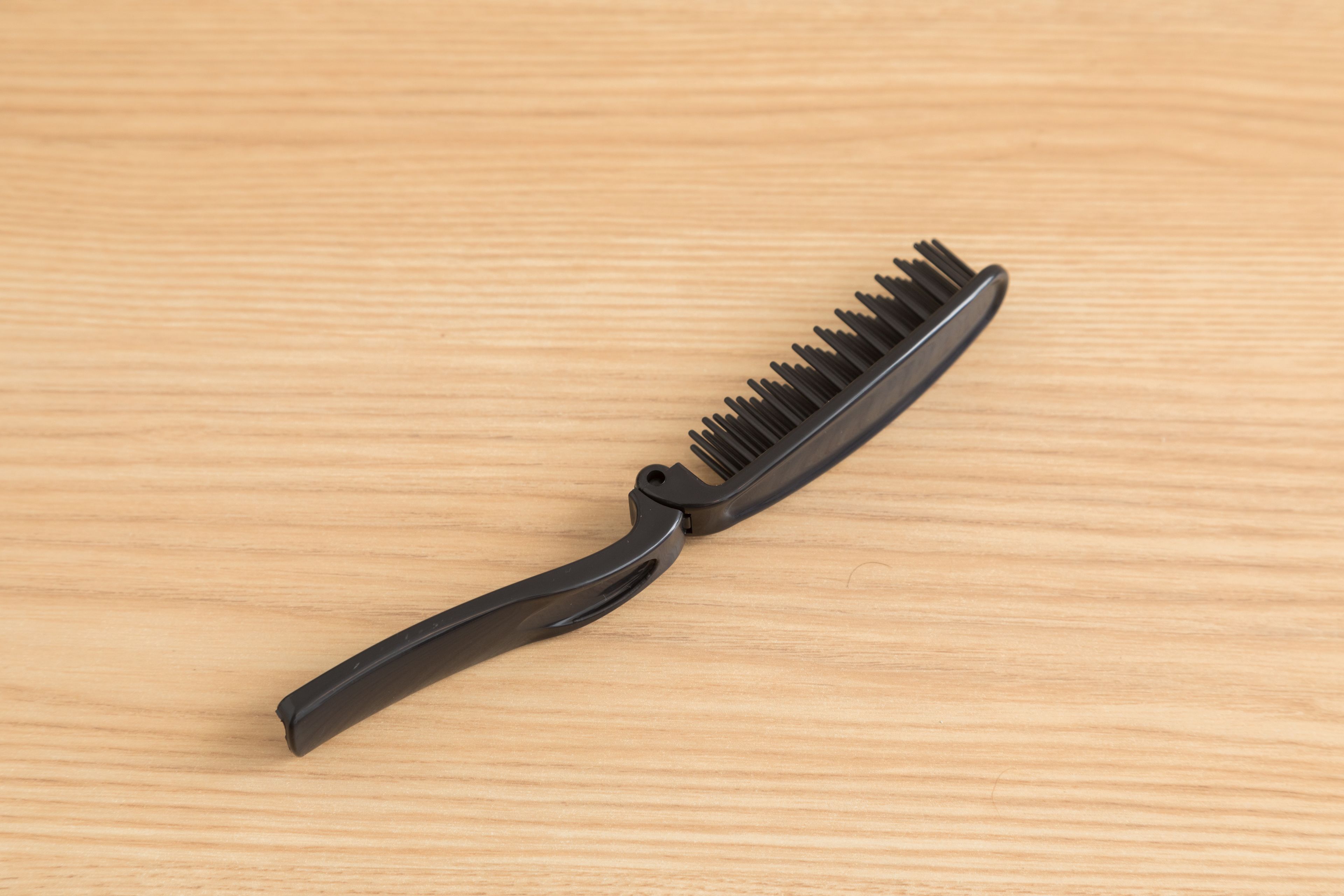 Une brosse à cheveux noire avec un manche, posée sur une surface en bois.