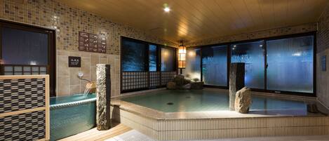 A traditional Japanese onsen with a wooden interior, a stone hot spring, and a tiled floor.