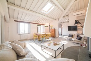 A spacious living area with a high ceiling, skylight, modern furniture, and a flat-screen TV.