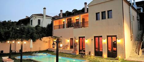 A two-story house with a swimming pool, outdoor seating, and a well-lit balcony.