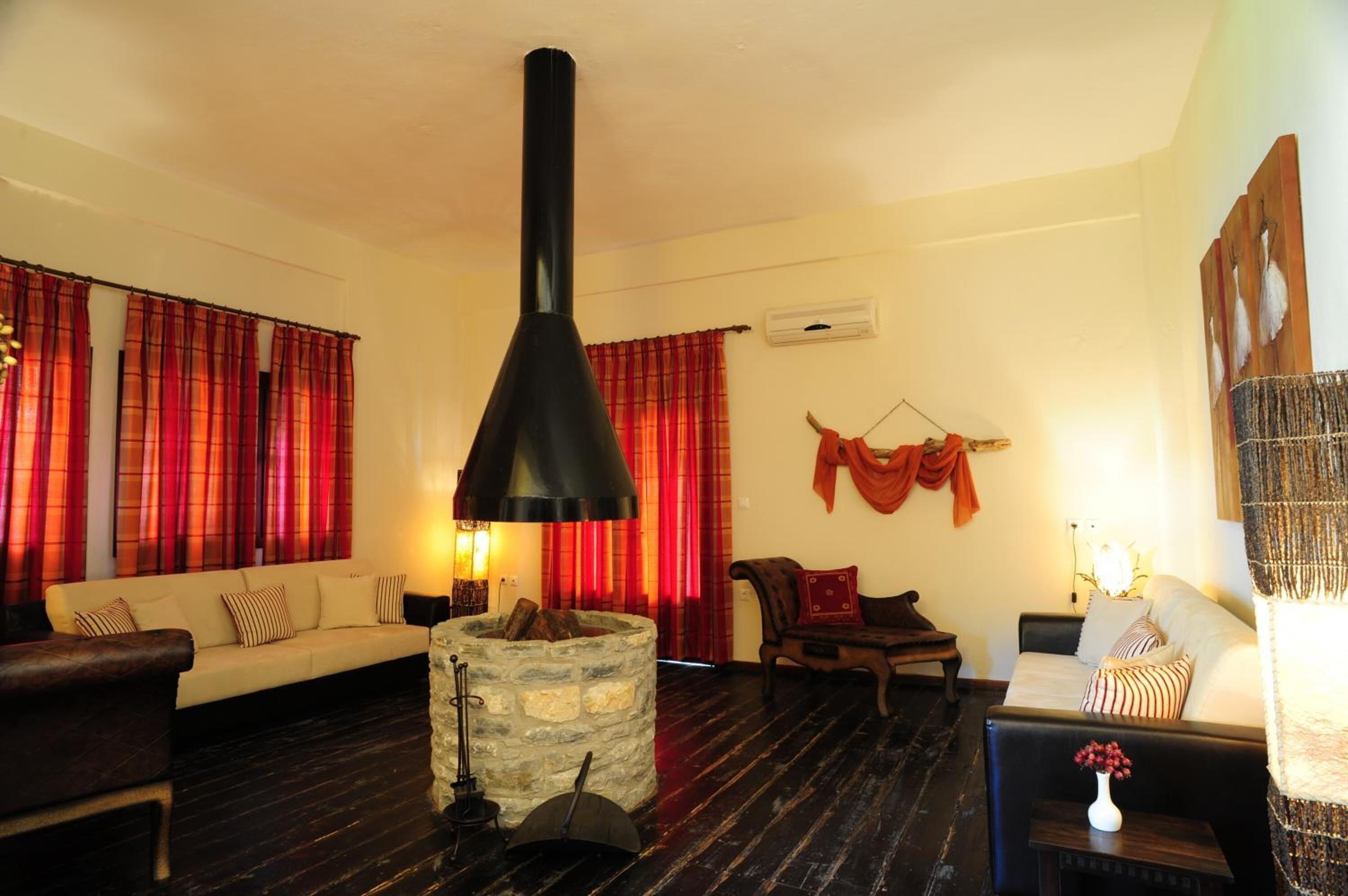 A cozy living room with a stone fireplace, red curtains, and a black chimney.