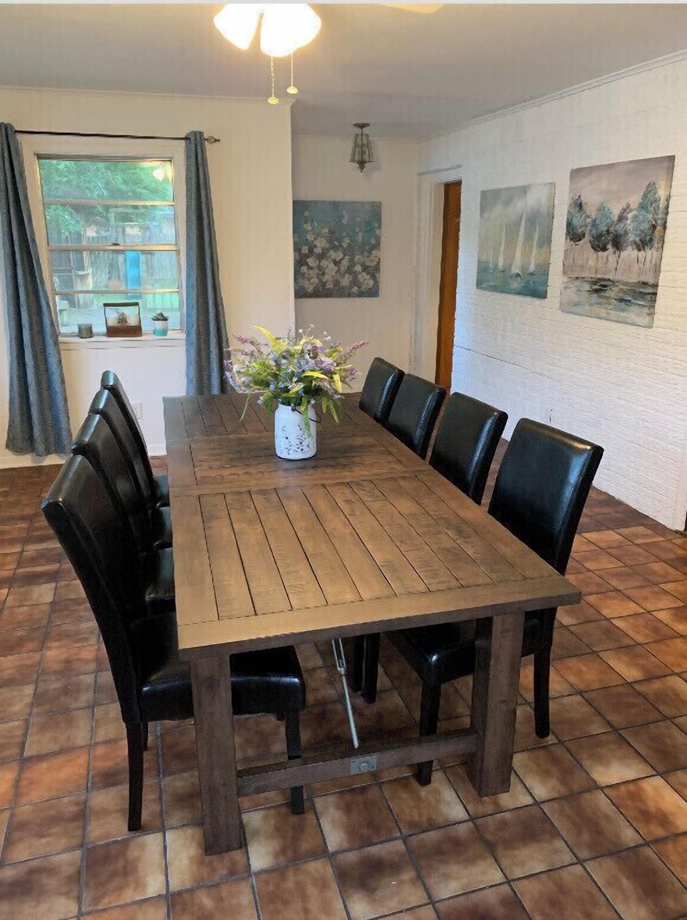 Une salle à manger avec une table en bois, des chaises noires, un vase rempli de fleurs et des œuvres d’art accrochées aux murs.
