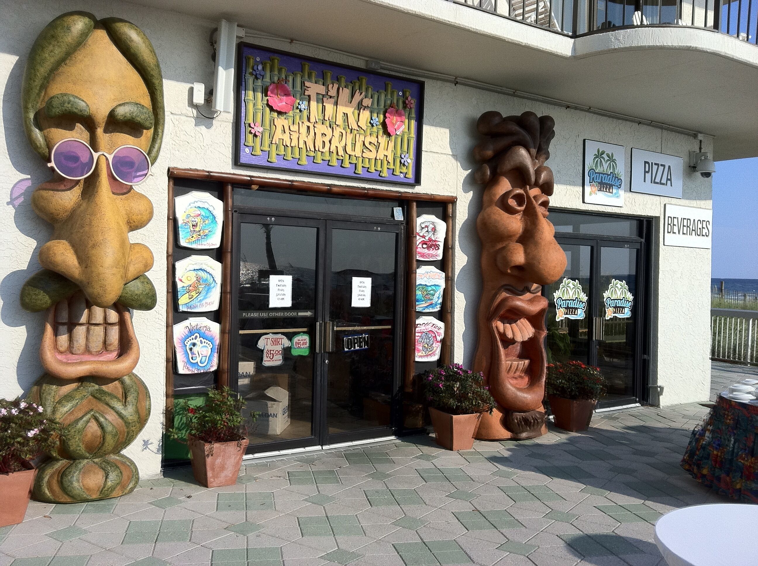 A storefront with a colorful sign, a large sculpture, and a sign for 'Paradise Pizza'.