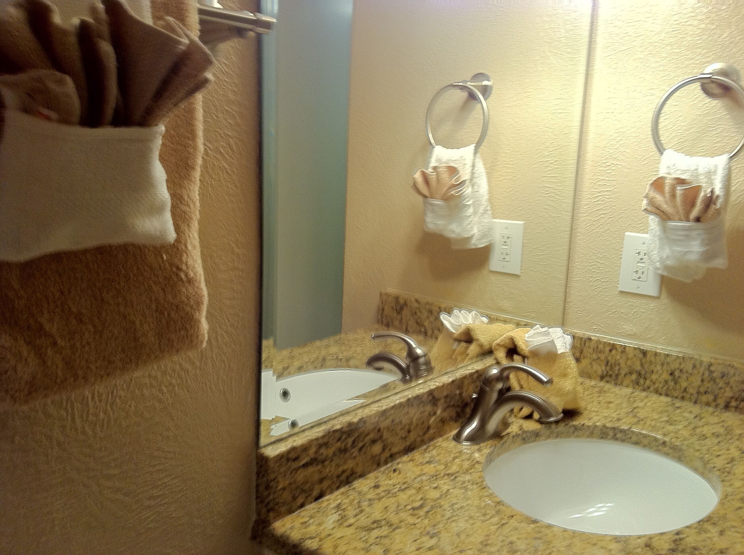 A bathroom with a sink, mirror, towel rack, and a towel dispenser.